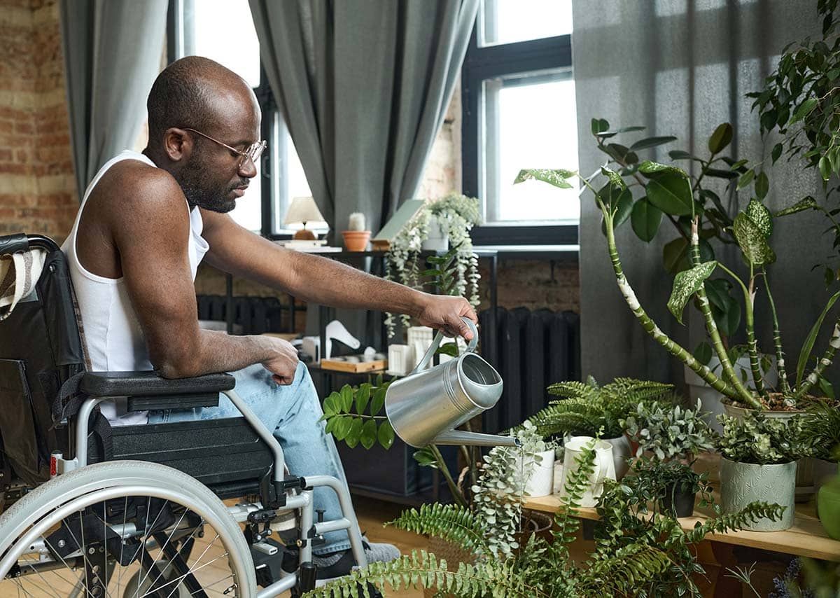 man in wheelchair watering flowers at home