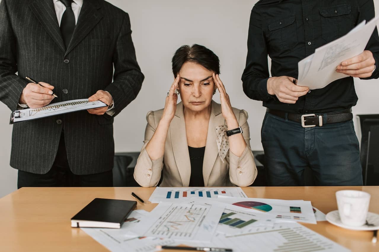 Woman sat at her desk, surrounded by paperwork. pressing her head due to stress