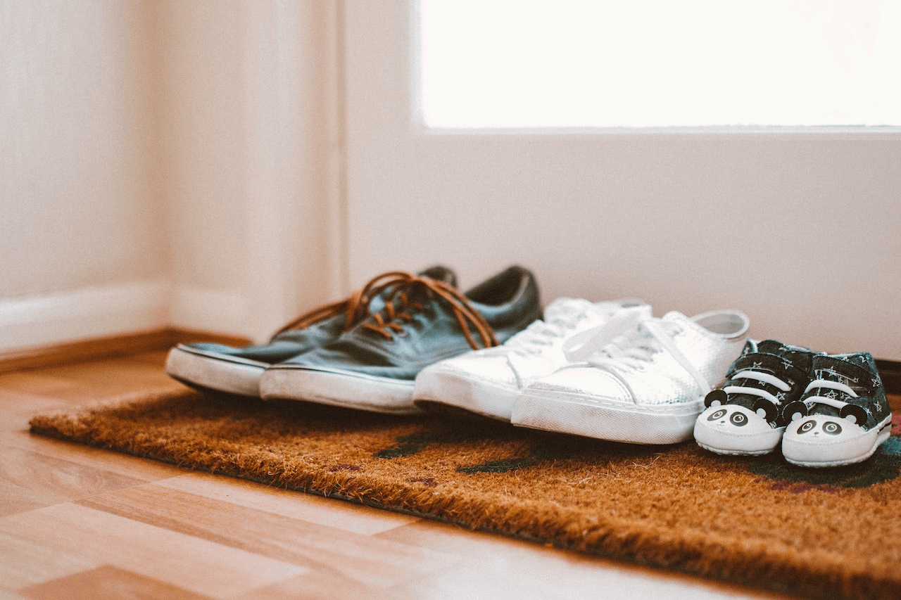 three pairs of shoes on a welcome mat by the front door