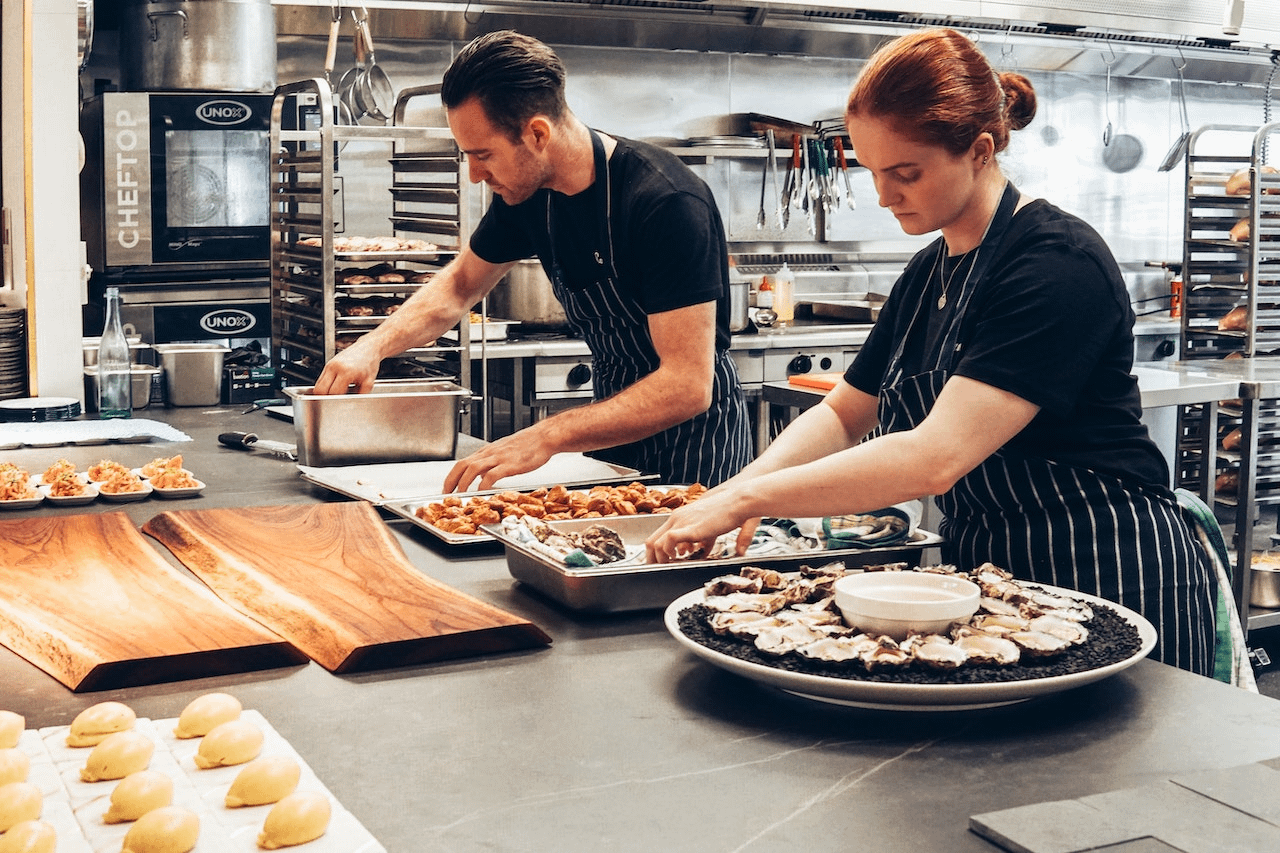 man and woman wearing black and white striped aprons in a restaurant kitchen