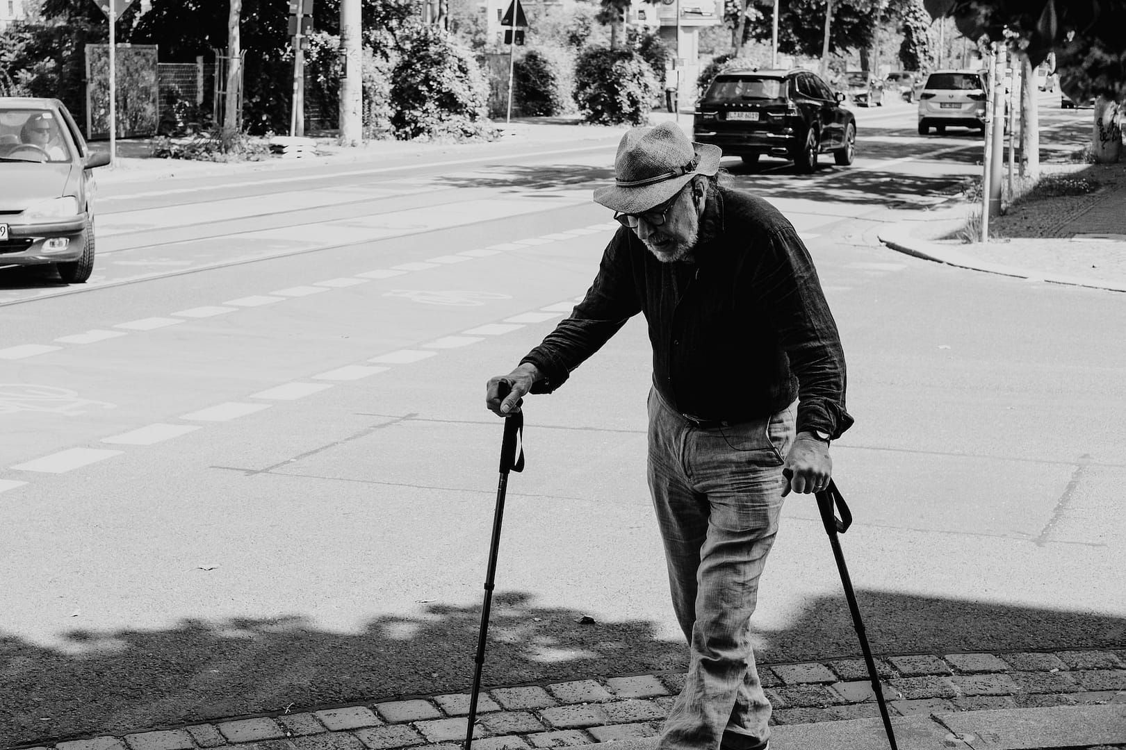 An older man using walking sticks in the street