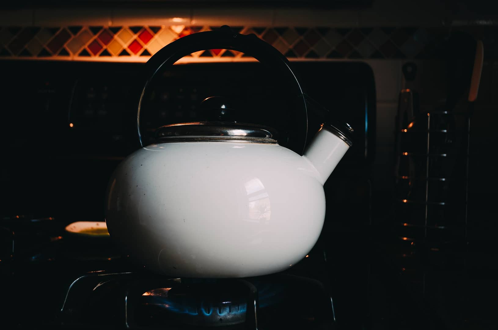 A white kettle being heated on a gas stove