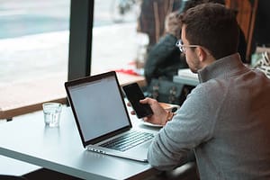 Man sitting at laptop with phone in hand