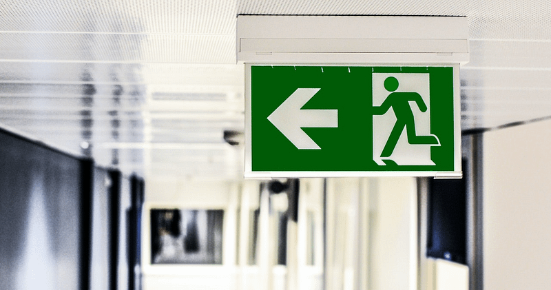 A green fire exit sign in a bright hallway