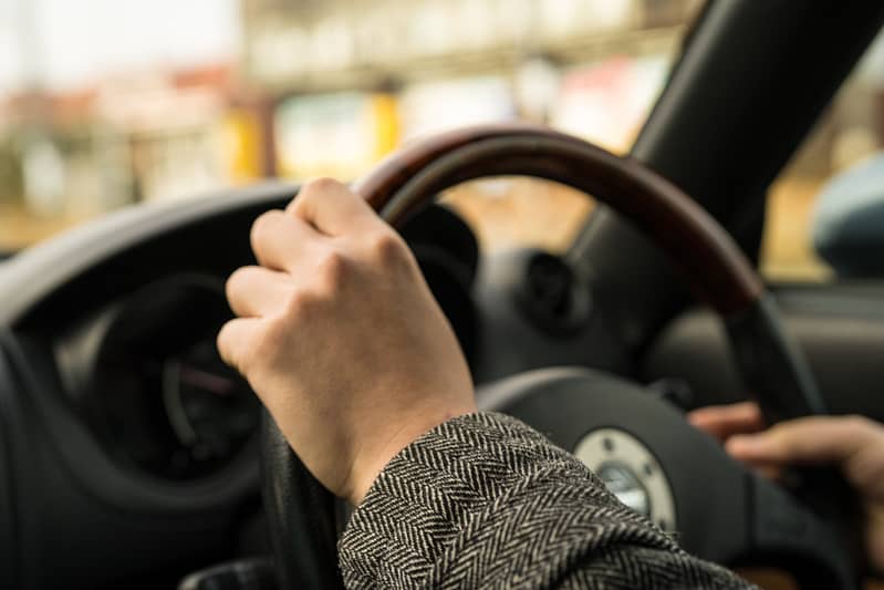 Close up of someone holding onto the steering wheel of their car