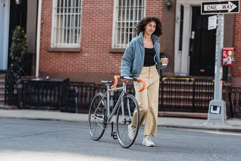 A teen crossing the road with their bicycle