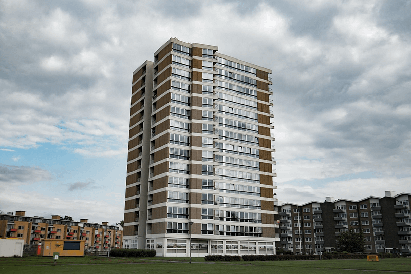 Image depicting a multi-story apartment complex with balconies and green spaces. The building is made of brick and concrete and has a modern design.