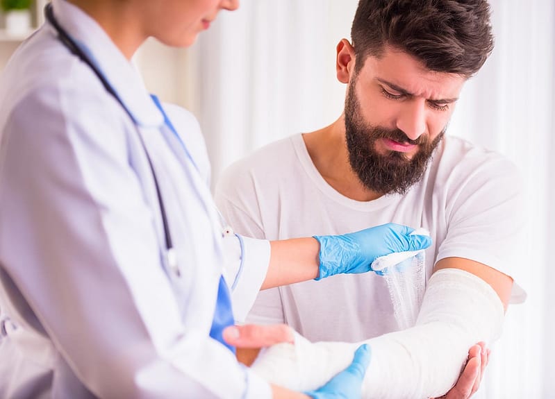 doctor bandaging man with arm injury